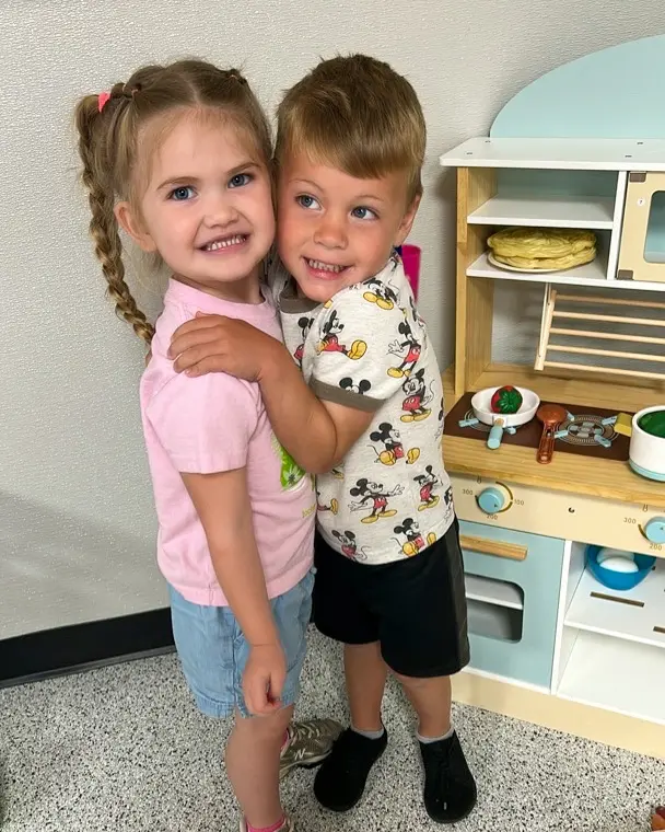 Two classroom friends hugging and smiling in front of their play kitchen at Skycrest