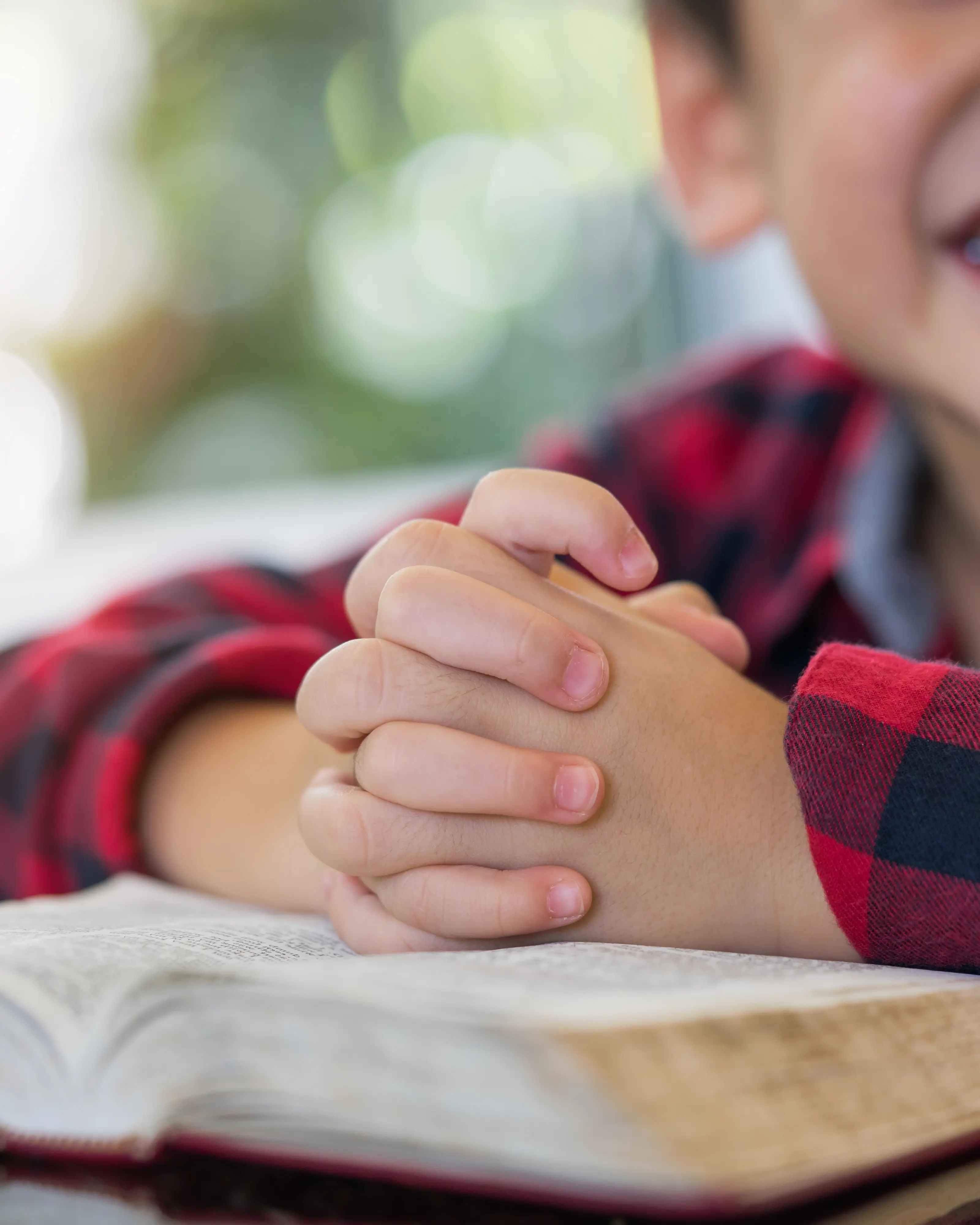 A child's folded hands resting in prayer on an open Bible