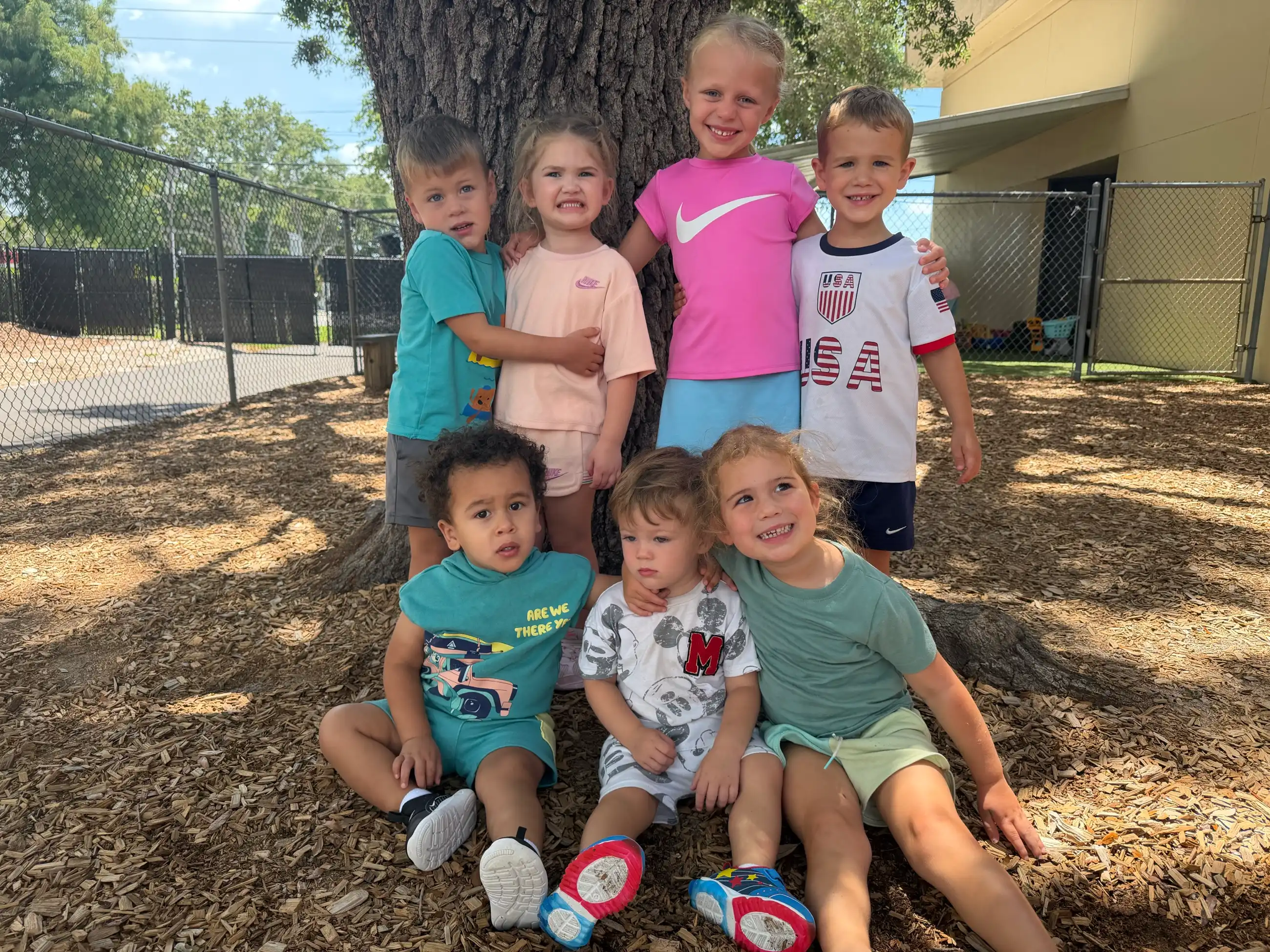 A joyful group of Skycrest students of all ages gathered together under the big oak tree on campus