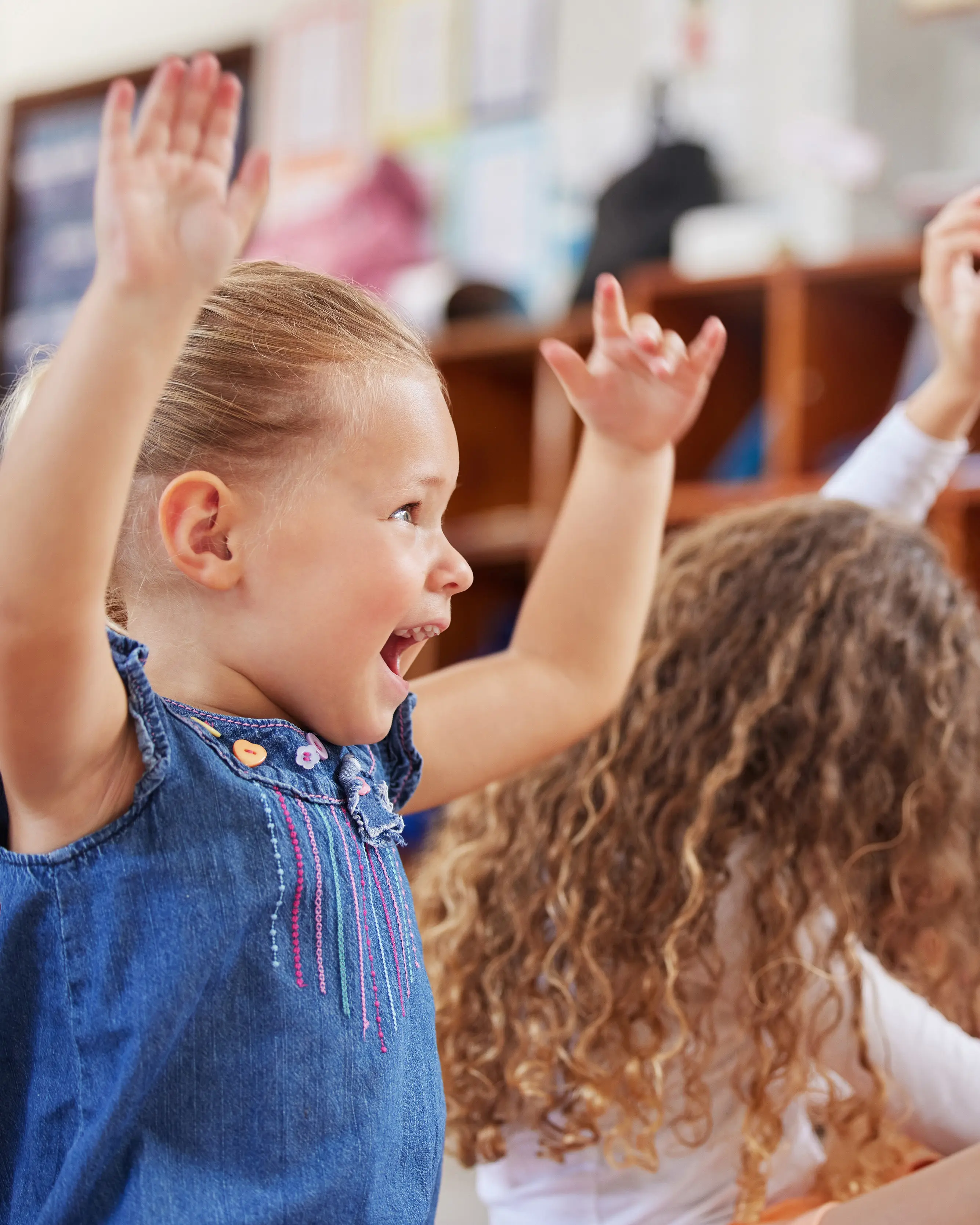 A joyful preschool girl raising her hands during a classroom activity